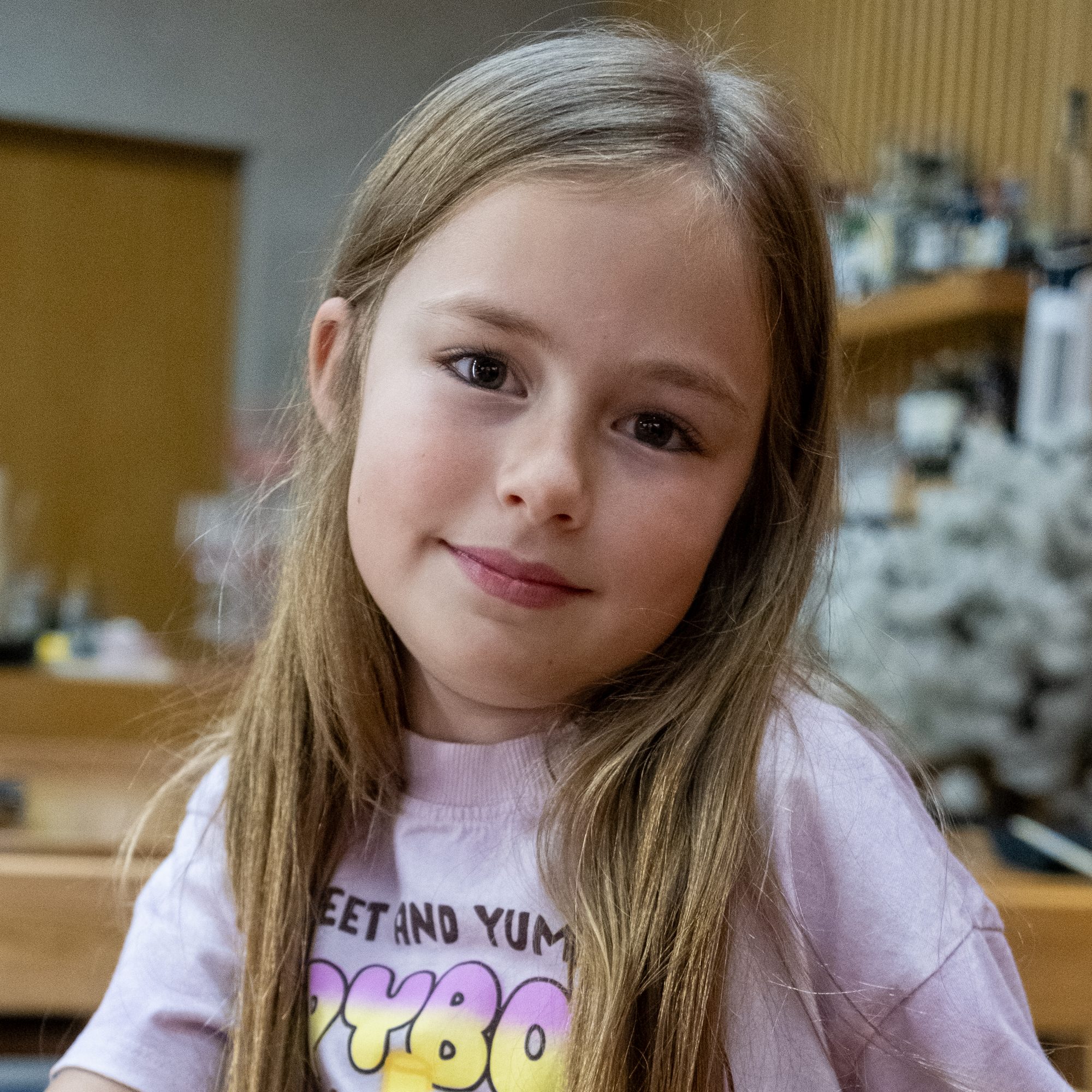 Portrait of a young girl with long hair in a pink T-shirt, smiling slightly.