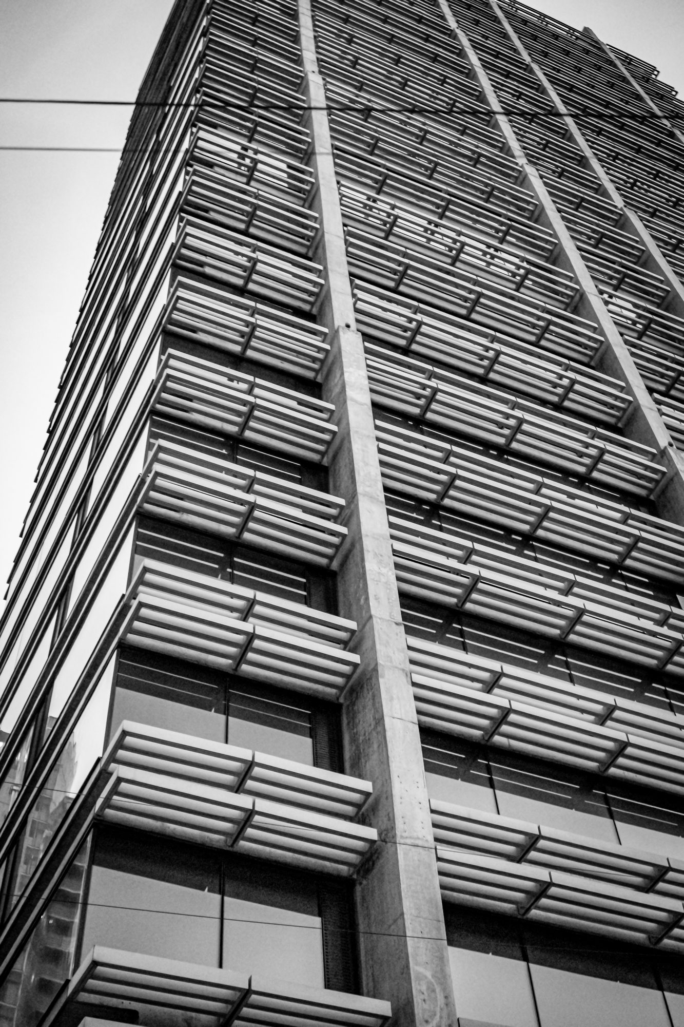Black-and-white view looking up a concrete tower wrapped in horizontal sunshade louvers.